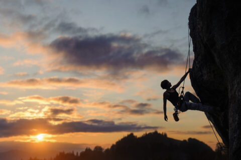 Silhouette of athletic woman climbing steep rock wall